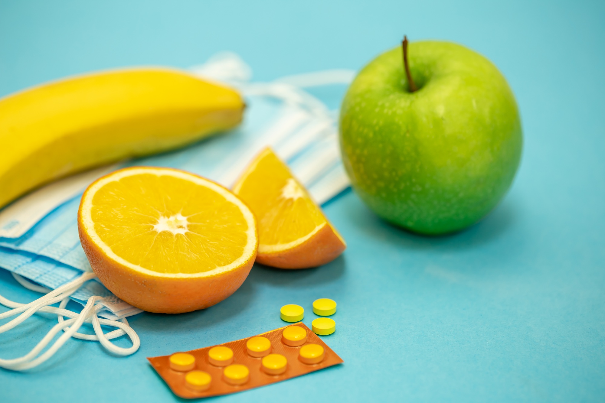 Fruits and pills on a blue background, disease prevention concept.